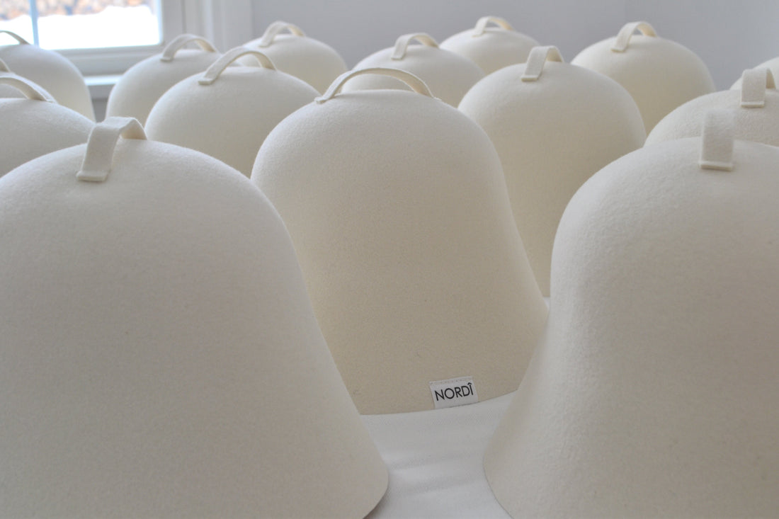 A collection of minimalist, undyed felted wool sauna hats with loops, featuring the signature NORDI label.
