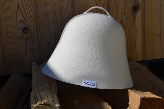 NORDI wool sauna hat resting on wood logs, symbolizing a peaceful and healthy sauna practice for longevity.