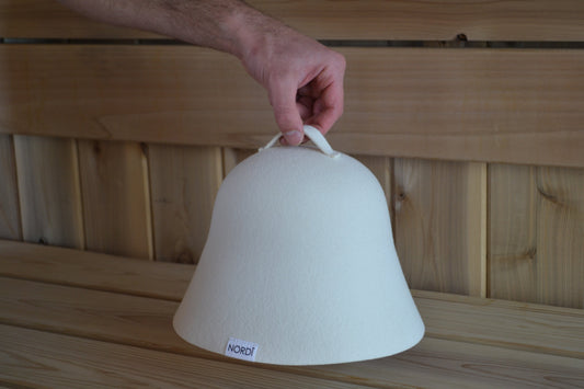 A signature NORDI wool sauna hat resting on a wooden bench in a dry Finnish sauna, highlighting the importance of head protection in high-heat environments.