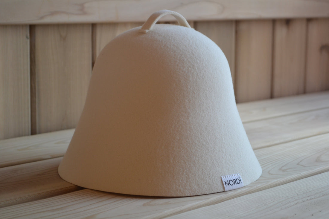 Undyed NORDI wool sauna hat made in USA resting on a wooden sauna bench, highlighting its use for hair protection and heat regulation.